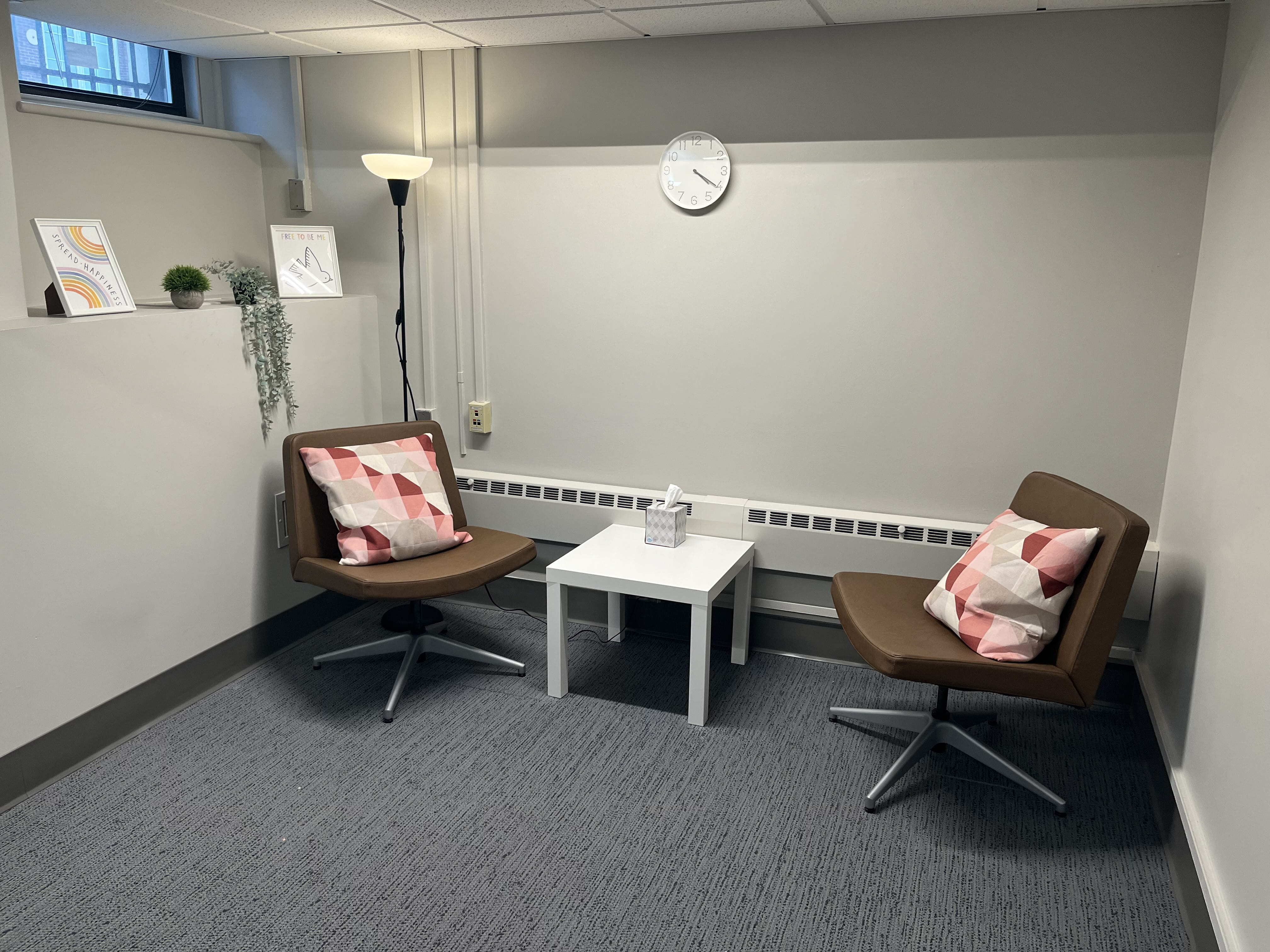 Two brown leather chairs with pillows are stationed around a table in a room with minimal decorations and plants.