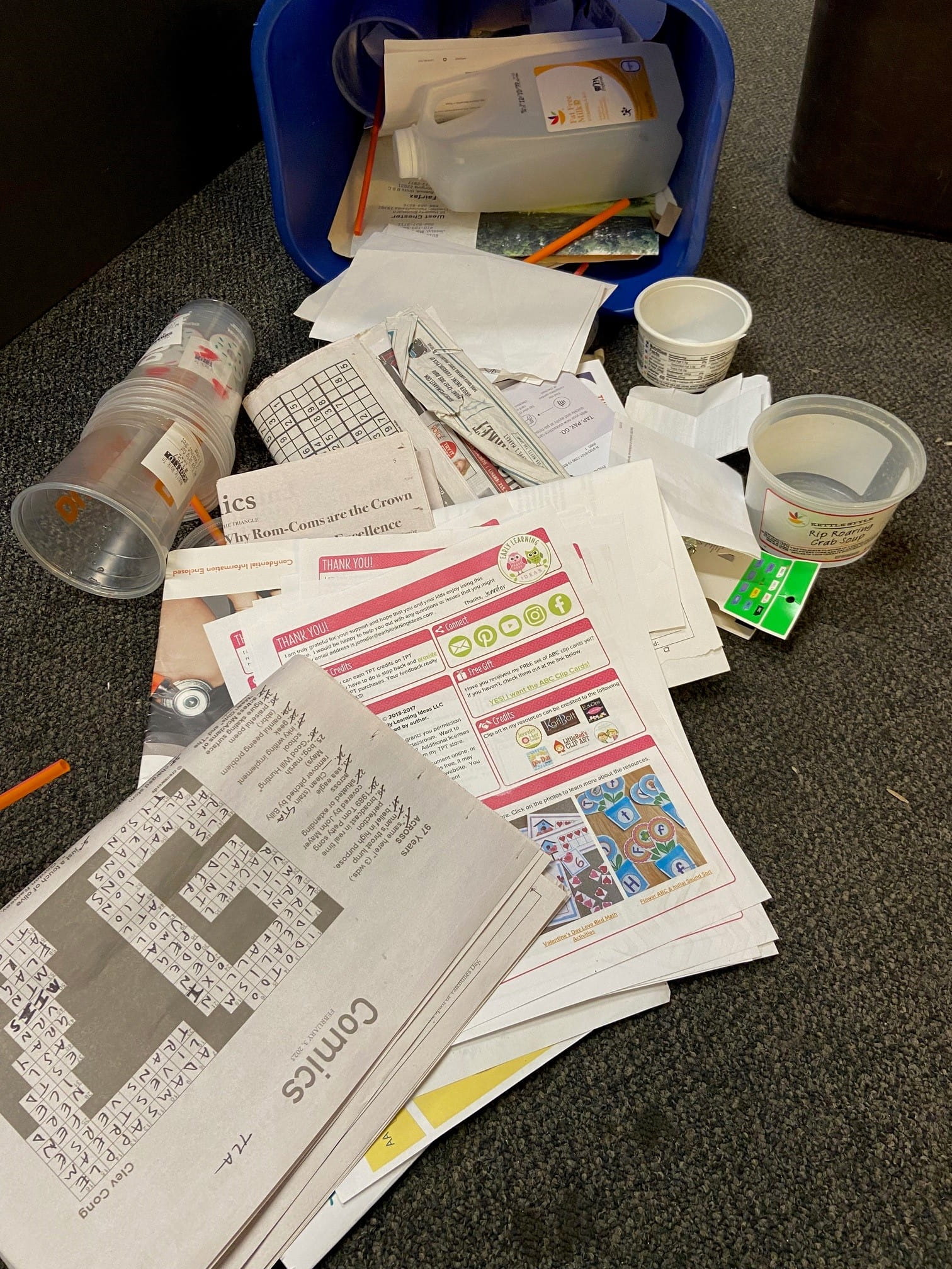 An overturned recycling bin with newspapers, papers and cleaned out plastic items.