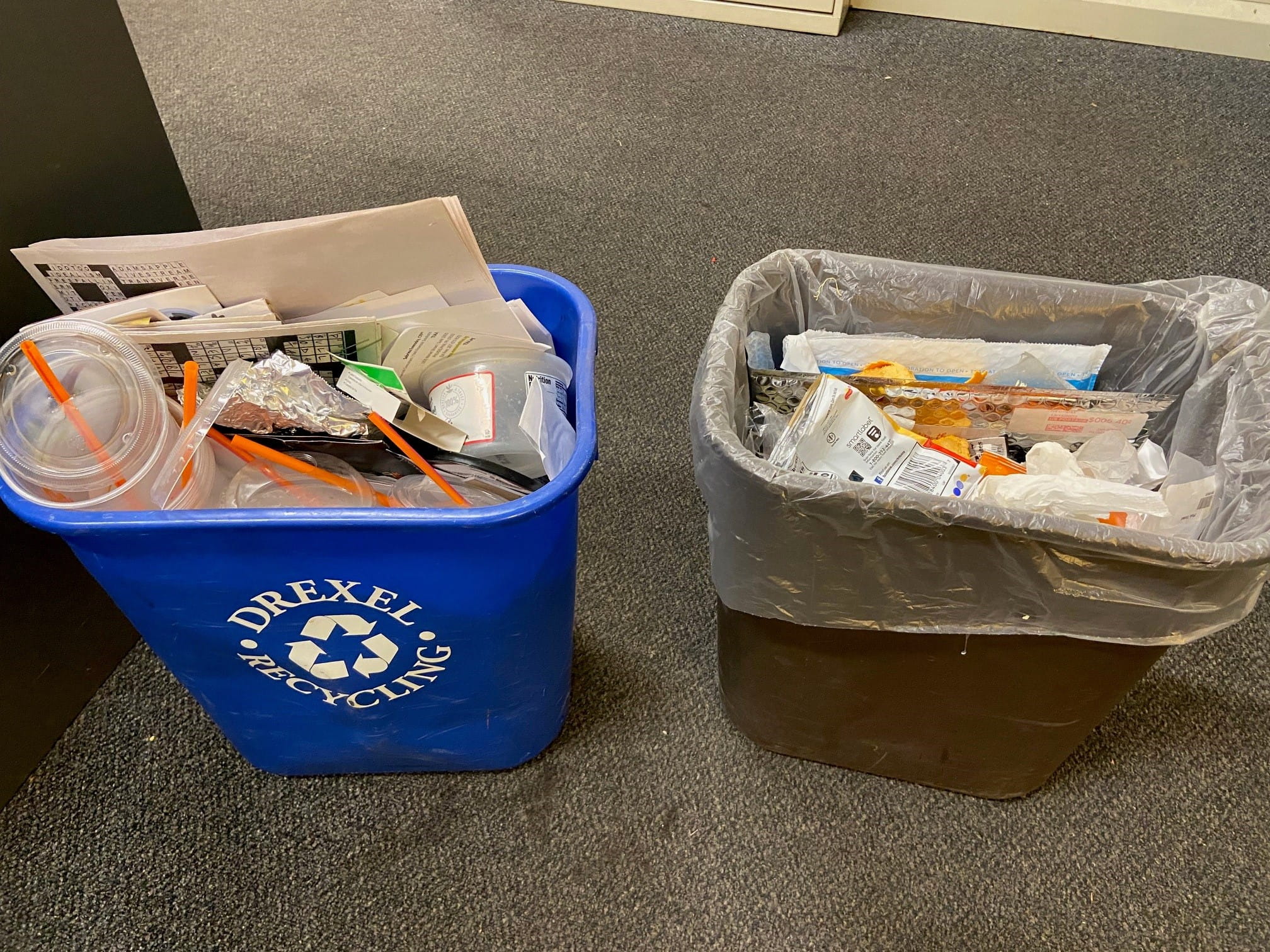 A filled blue recycling bin next to a filled trash can.