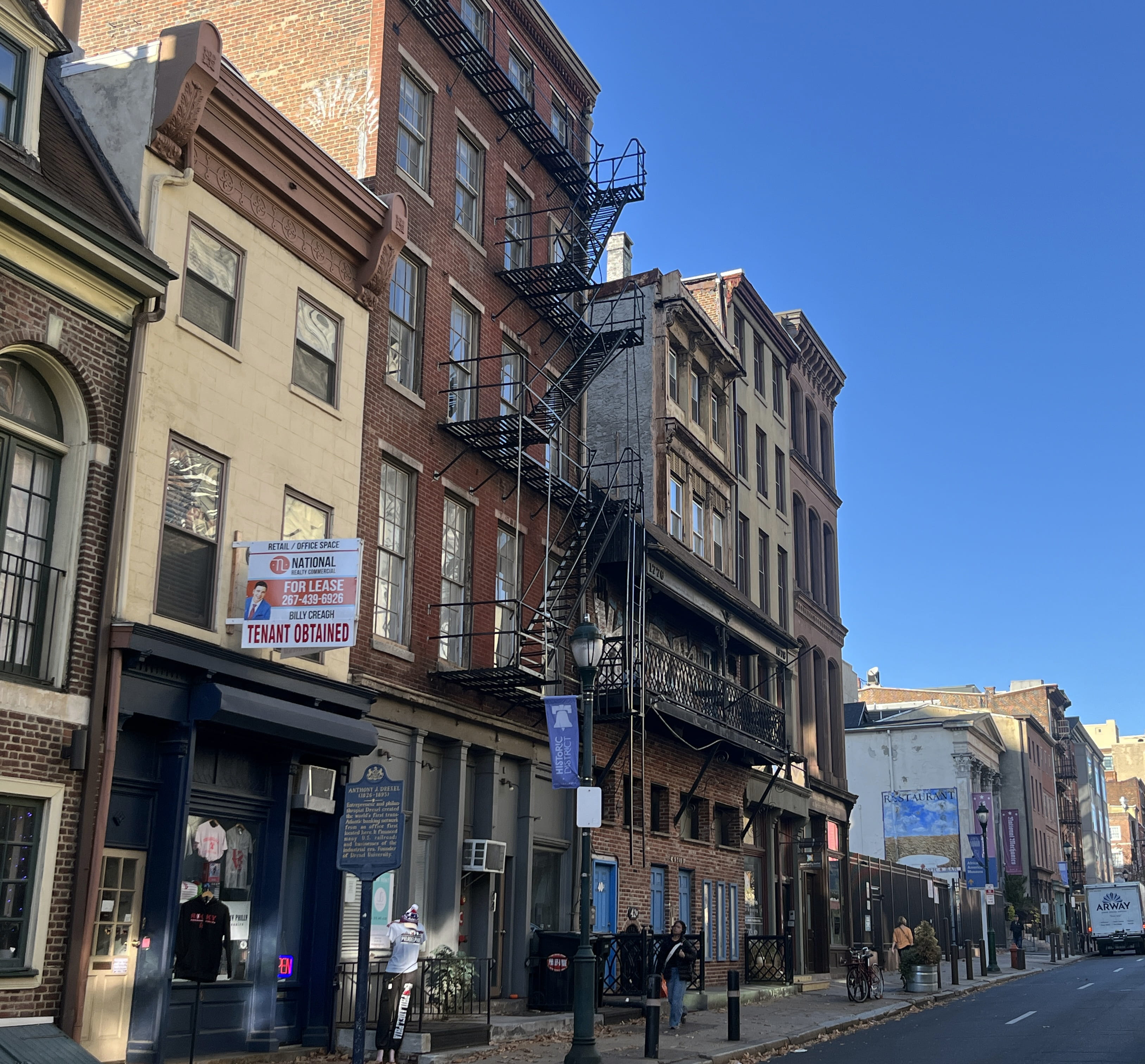The view of Third Street, Philadelphia’s former financial epicenter, containing two former locations of Drexel & Co. The 1838 location is the navy and yellow building with the historical marker for Anthony J. Drexel. The 1854 location is the parking lot behind the black fence.